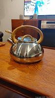 Side view of stainless steel whistling kettle with faux wood handle, showing the spout and lid