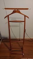 Front view of the gentleman's floor stand showing built-in wooden hanger, small shelf, and horizontal bar with hooks.