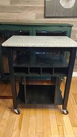 Front view of the moveable kitchen cart showing granite top, cubbyhole storage underneath, and lockable wheels.