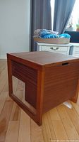 Side angle showing boxy shape, wood grain sides, framed base and top lid which lifts for storage.
