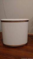 Front view of mid century modern laundry hamper showing white body and gold horizontal trim.