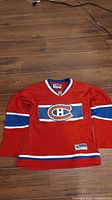 Full view of the red Montreal Canadiens youth hockey jersey laid flat to display front, showing logo, striping, and collar detail.