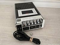 Front view of Superscope 3 Head cassette player with visible cassette compartment, control buttons, power cord, and loose knob in foreground.