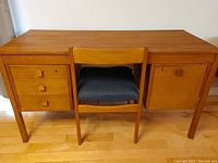 Full front view of teak desk with three drawers on the left and a door on the right, with chair placed in front