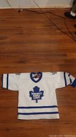 Full front view of white kids large Toronto Maple Leafs hockey jersey with blue trim and logo.