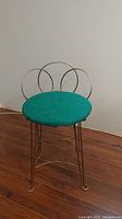 Front angle view of vintage metal chair with green seat and circular hoop backrest showing metal legs and curved foot supports.