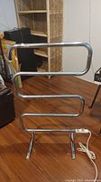 Front view of the freestanding vintage electric towel warmer with chrome finish and serpentine tubular design on a wooden floor.
