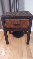 Front view of the wicker end table showing dark wicker woven top and sides, and a front drawer with natural brown wicker weave and handle.