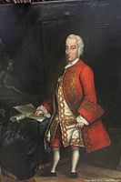 Full view of the portrait painting showing the gentleman in red Rococo attire in standing pose beside a table with documents.
