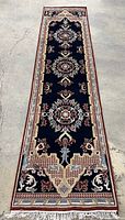Full view of navy runner with border edges and fringed ends laid on concrete floor.