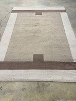 Full view of rectangular beige, cream, and brown geometric modern carpet on concrete floor.