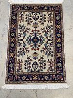 Full view of small rectangular hand-knotted rug showing cream field with floral motifs, navy border and fringed edges
