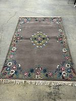 Full view of rectangular rug on concrete floor showing overall floral border and central medallion