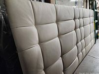 Side angled view of beige leatherette king size headboard showcasing padded tufted square panels.