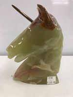 Front view of polished marble unicorn bust with bronze-colored horn, showing green and brown marble coloration.
