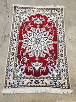 full view of red field Persian rug with cream border and fringe laid on concrete