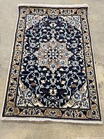 Overall view of navy blue Persian rug with central medallion pattern on concrete floor