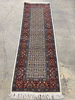 Full view of Persian hand knotted runner on concrete floor showing full length and fringe.