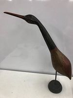 Side view of the wooden bird showing painted black head and neck, and natural wood body mounted on a black metal base.