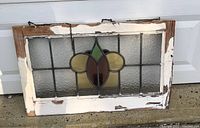 Photo of antique leaded stained glass window in worn wooden frame, showing front view resting on concrete