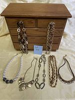 Photo showing wooden jewelry box with multiple drawers and six necklaces laid out in front.