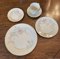 Set of Lenox Heiress china showing floral and gold trimmed dinner, salad, bread plates, cups and saucers arranged on a wooden surface.