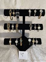 Photo showing a lot of 15 ladies wristwatches arranged on a black display stand with three tiers, featuring differing band styles and watch faces.