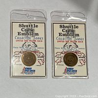 Front view of two solid bronze shuttle coins sealed in clear plastic sleeves with printed backing cards showing 'Shuttle Crew Emblem Collection Series' and Kennedy Space Center logo.