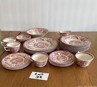 Full set of 29 pieces including plates, bowls, cups, saucers, creamer, and serving bowl with a crack. All items have maroon floral Tonquin pattern on cream porcelain.