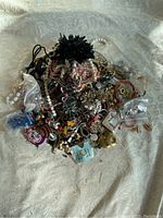 Top view of a pile of assorted costume and fashion jewelry including necklaces, bracelets, earrings, rings, brooches and pendants on fabric background.
