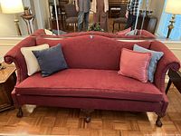 Front view of the cranberry red camel back couch showing cushions and carved wooden legs.