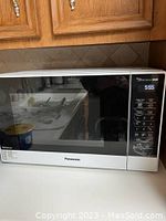 Front view of Panasonic microwave oven placed on kitchen counter under wooden cabinets, showing control panel and door with black window.