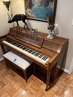 Front left angle of upright piano showing keyboard, music rack and bench