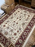 Full view of rectangular area rug showing ornate floral pattern in burgundy, beige, and taupe tones with visible underpad underneath the rug