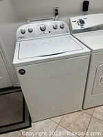 Whirlpool washer and partial view of Kenmore dryer side by side on tiled floor