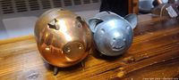 Side view of brass-colored and silver-colored metal piggy banks on wooden surface.