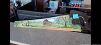 Side view of antique hand saw showing landscape painting on blade and wooden handle