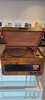 Front view of antique wooden radio and turntable with lid open, showing turntable and tonearm inside.