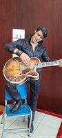 Front angle showing Elvis Presley doll playing guitar while standing on chair with ELVIS sign