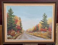 Front view of the framed oil painting showing a road with autumn trees on both sides under a clear blue sky.