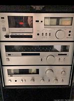 Three silver-front Sansui components stacked inside cabinet