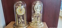 Front view of two dome clocks under glass covers on wooden surface