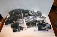 Photo showing multiple resealable plastic bags containing black batteries of various sizes for handheld amateur radios, arranged on a white surface with a white background.