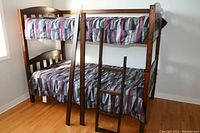 Photo showing solid wood bunk bed with two mattresses and bedding, including a ladder leaning against the bed frame