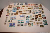 Large assortment of mostly unused stamps with various themes and from multiple countries spread out on a flat surface.