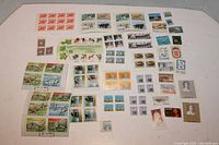 Top view showing large assortment of Canadian and US collectible postage stamps, blocks and singles arranged on white background.