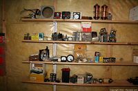 Shelf with various electrical components including analog meters, fans, transformers, relays, and boxes of contact switches.