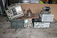 Photo showing a group of vintage electronic test devices including oscilloscopes, meters, and a wooden mounted transformer.