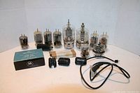 Overview photo showing various vintage radio tubes, black cylindrical tube, Motorola MS-15 heat sink in original box, black plastic tube sockets, and a power cord.