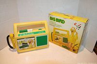 Front view of yellow vintage cassette player with Big Bird image and green speaker grill, accompanied by original colorful box featuring Big Bird and musical notes.
